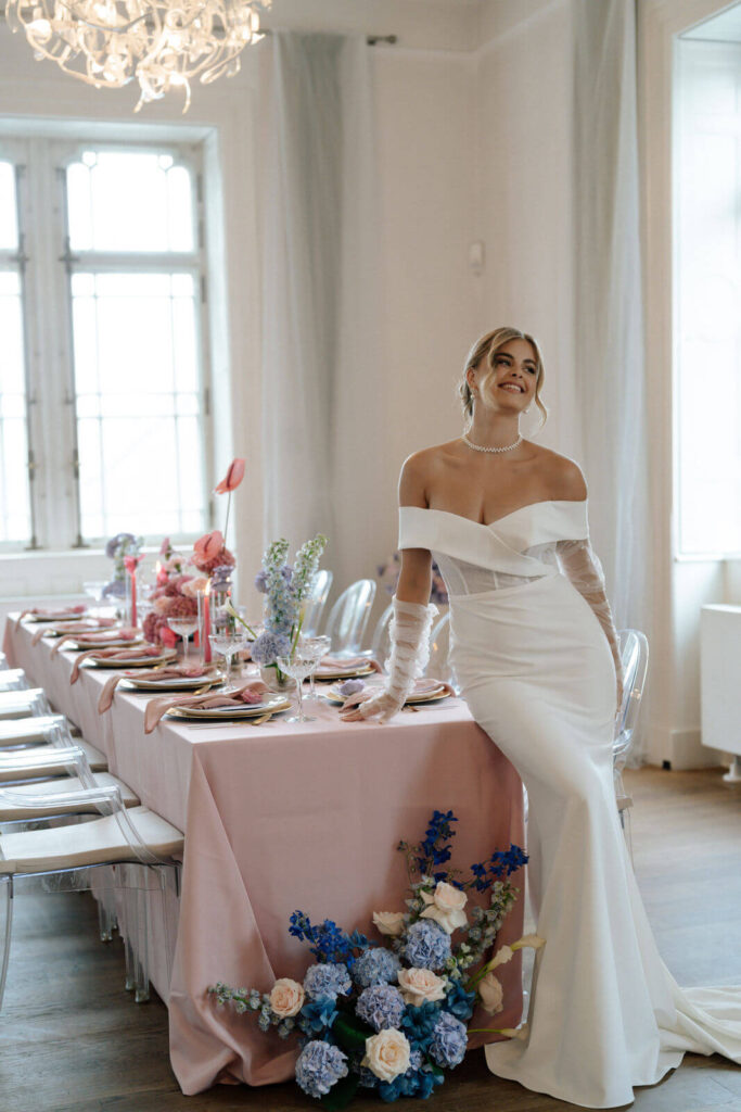 Braut in elegantem, weißen Brautkleid gekleidet, steht vor einem eleganten dekorierten Tisch mit rosa Tischdecke.
