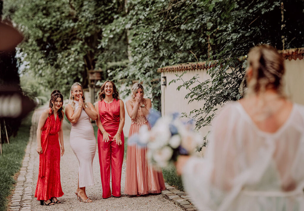 Brautjungfern sehen braut zum ersten Mal im Brautkleid und lachen emotional.