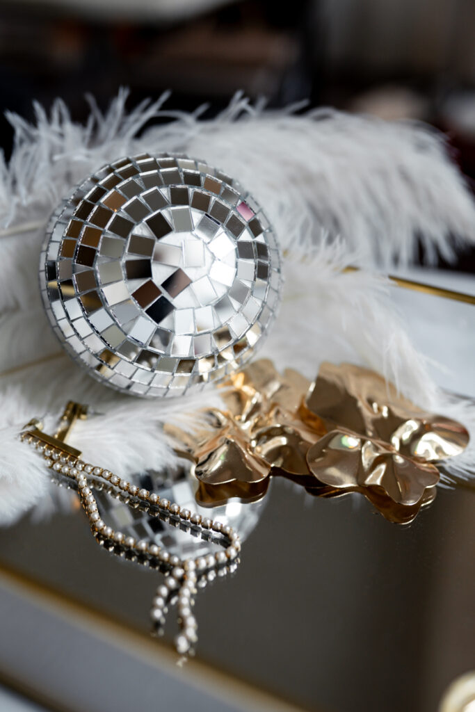 silberne kleine Discokugel liegt neben Kette und goldner Ansteckbroche.